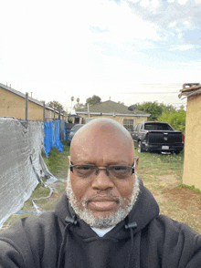 a man wearing glasses and a black hoodie takes a selfie in front of a blue tarp