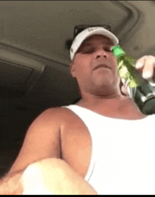 a man in a white tank top is holding a green bottle .