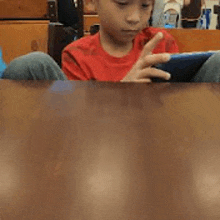 a young boy is sitting at a table playing a game on a cell phone .