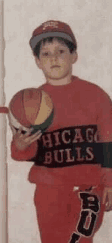 a young boy is holding a basketball in his hand while wearing a chicago bulls sweater .