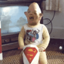 a baby is wearing a superman shirt and riding a superman toy .