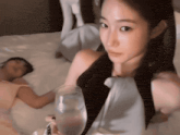 a woman is holding a glass of water while a man sleeps on a bed