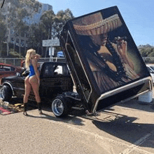 a woman is standing next to a lowrider car with the hood open .