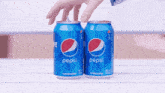 two cans of pepsi on a table with a person opening one