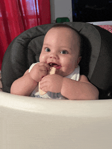 a baby is sitting in a high chair and chewing on a piece of bread