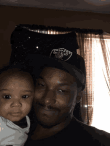 a man wearing a raiders hat holds a baby in his arms