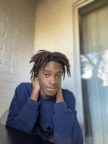 a young man with dreadlocks is sitting at a table with his hands on his face