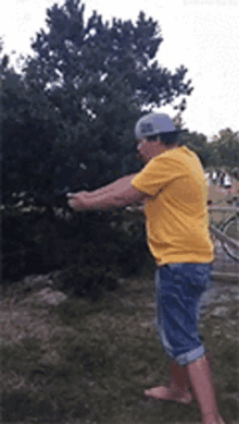 a man in a yellow shirt and blue shorts is standing in the grass with his arms outstretched