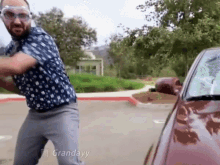 a man wearing glasses is standing in front of a red car with the words grandayy written on the bottom