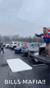 a man is jumping over a table in a parking lot with the words `` bills mafia '' .