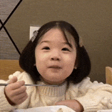 a little girl is sitting at a table with a plate of food and a fork in her hand .