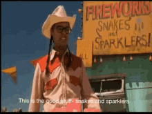 a man in a cowboy hat and glasses stands in front of a sign that says fireworks snakes and sparklers