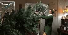 an elf is holding a christmas tree in his hands in a living room .