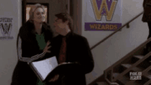 a man and a woman are standing in front of a w wizards sign