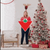 a woman is holding a red triangle with a maple leaf on it in front of a christmas tree .