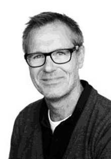 a man wearing glasses is smiling in a black and white photo .