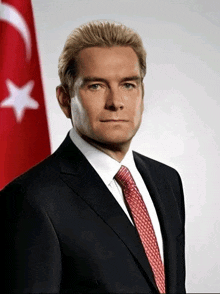 a man in a suit and tie stands in front of a red and white flag