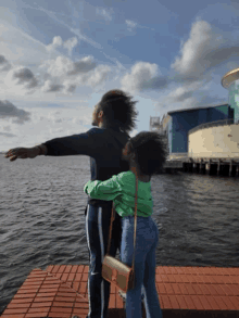 two people standing on a dock with their arms outstretched in front of the water