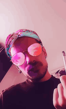 a man wearing sunglasses and a bandana is smoking a cigarette and giving the middle finger