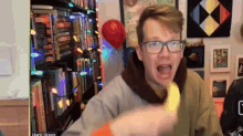 a man wearing glasses is eating a banana in front of a bookshelf with hank green written on the bottom