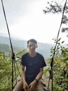 a young man wearing glasses and a black shirt with a smiley face on it sits on a swing