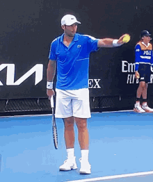 a man holding a tennis ball and a racket on a tennis court in front of a sign that says emirates