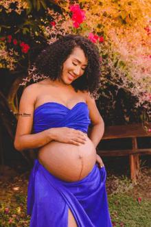 a pregnant woman wearing a blue dress has a tattoo on her arm that says ' lion '