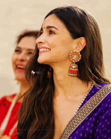 a woman wearing a purple top and earrings smiles