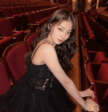 a woman in a black dress sits in an auditorium with red seats