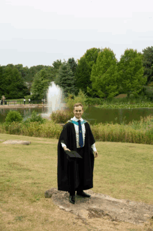 a man in a graduation cap and gown stands in front of a pond