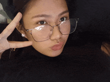 a woman wearing glasses makes a peace sign with her hand