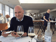 a man sitting at a table with two glasses of wine and a bottle of water