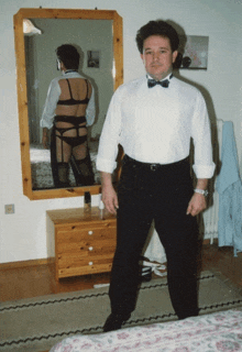 a man in a bow tie stands in front of a mirror with a woman in lingerie behind him