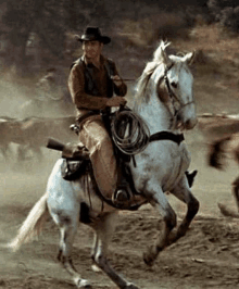 a man in a cowboy hat is riding a white horse with a gun on the back .