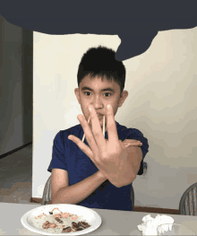 a young boy is sitting at a table with a plate of food and chopsticks in his mouth