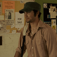 a man wearing a hat is standing in front of a bulletin board with missing and for sale signs on it