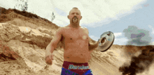 a shirtless man in a duralast shorts is holding a brake disc