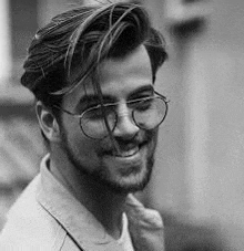 a black and white photo of a man with glasses and a beard .