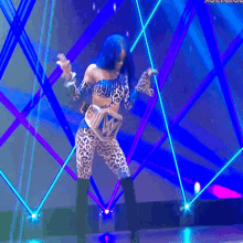 a woman in a leopard print outfit is dancing on a stage with a blue background .