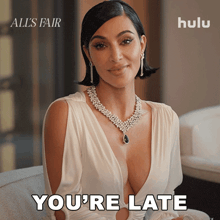 kim kardashian is wearing a white dress and a necklace with the words you 're late below her