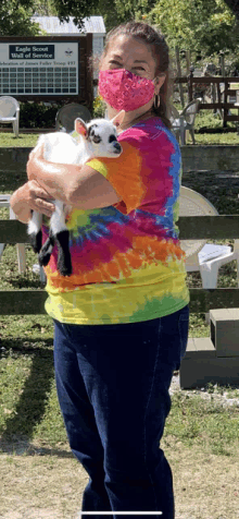 a woman wearing a tie dye shirt is holding a goat