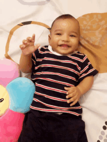 a baby wearing a striped shirt is laying on a bed next to a stuffed animal