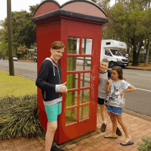 two boys and a girl standing in front of a red phone booth that says mail