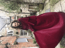 a woman in a long red dress is standing in front of a stone building