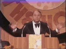 a man in a tuxedo stands at a podium with his arms outstretched in front of a sign that says historic