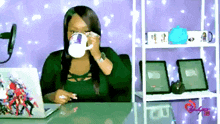 a woman sitting at a desk drinking from a mug with a picture of a person on it