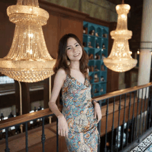 a woman in a blue dress is standing on a railing in front of a chandelier