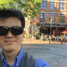 a man wearing sunglasses and a blue shirt is taking a selfie in front of a restaurant .