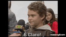 a young boy with curly hair is talking to a reporter while standing in front of a crowd of people .