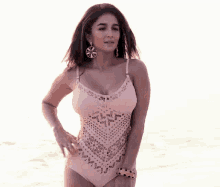 a woman in a pink swimsuit and earrings stands on the beach